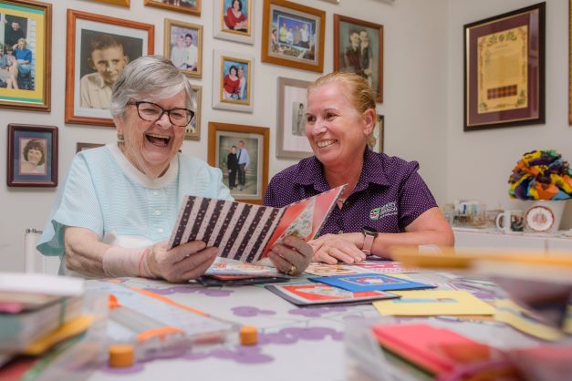 Lady laughing whilst going through cards and memories with her care worker Home care worker celebrating a residents birthday