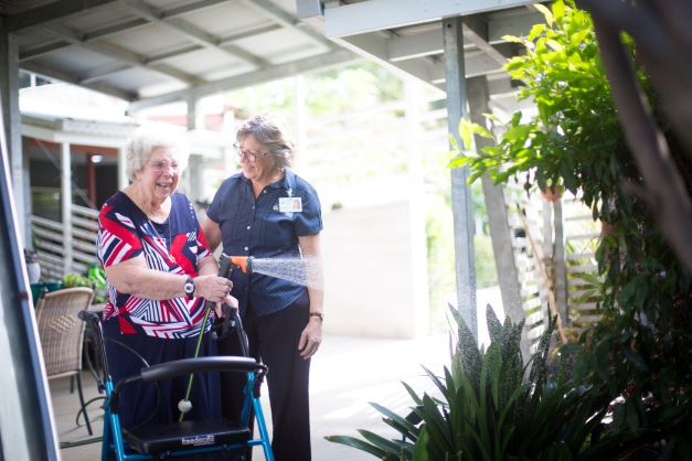 Female resident hosing the gardens and smiling with staff member Resident watering the garden at Anam Cara